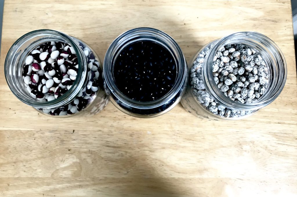 three jars of dried beans viewed from above on light wood