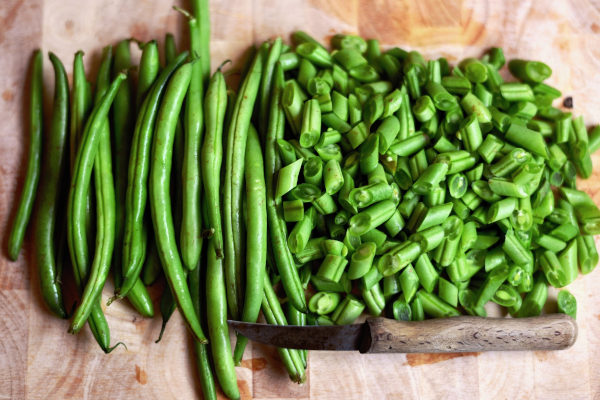 whole and chopped green beans with knife on wooden cutting board