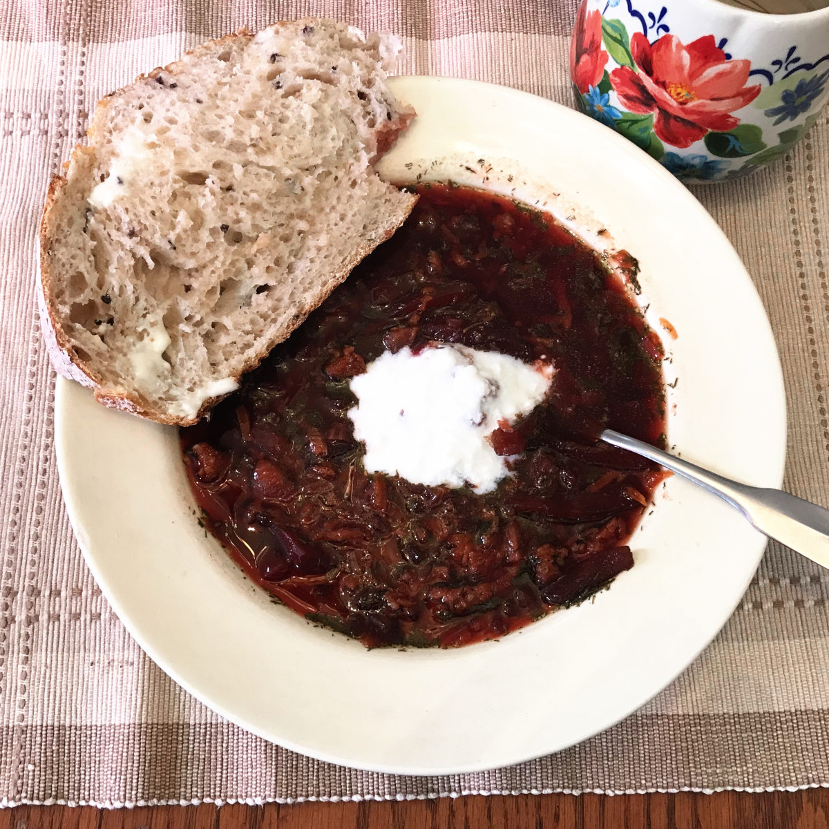 Bowl of beet soup on placemat with slice of bread