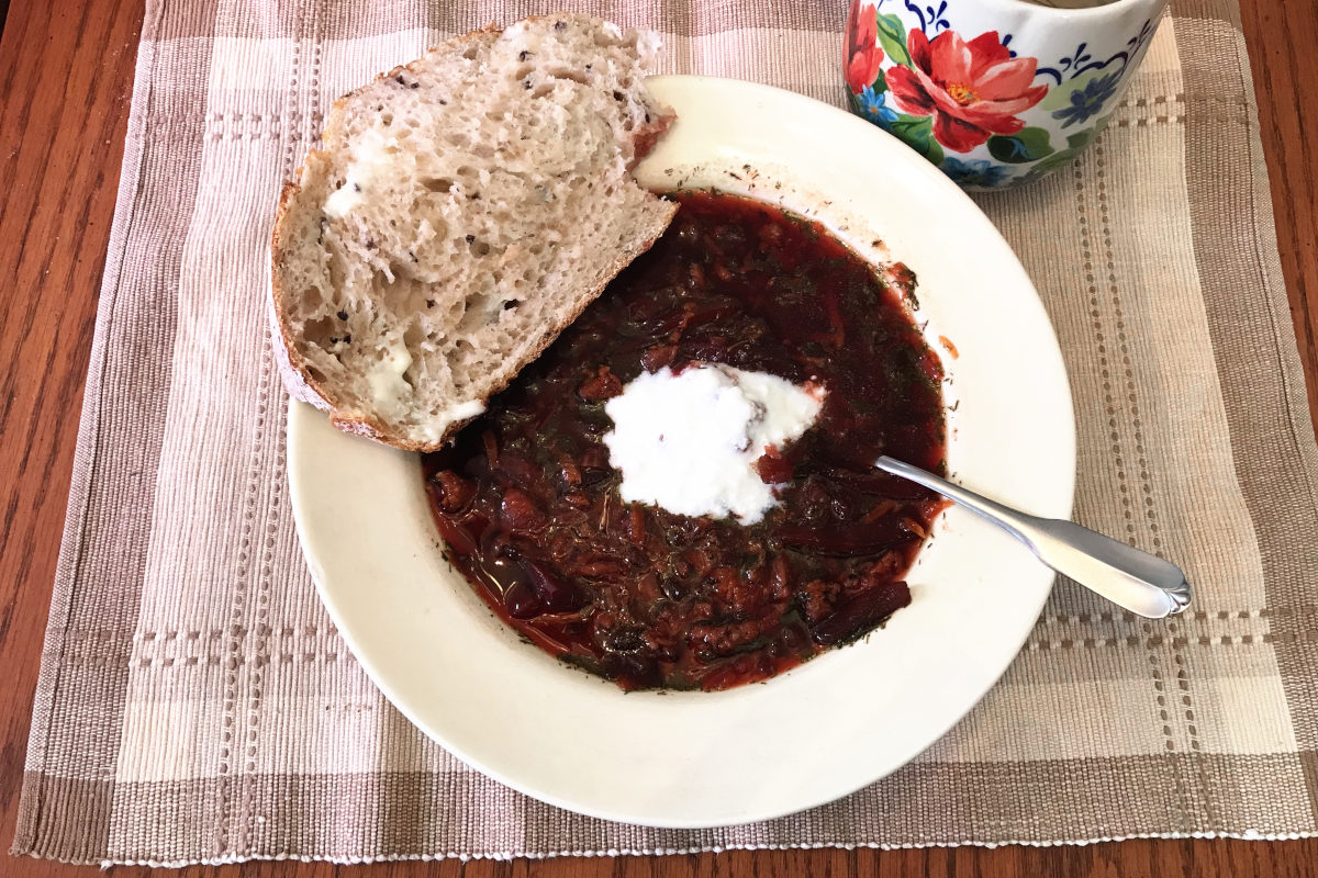 beet soup in bowl on placemat with slice of bread