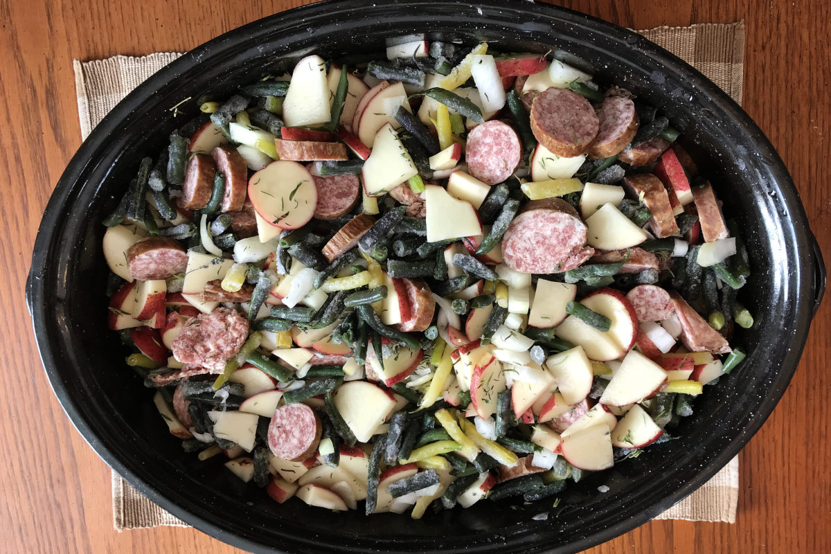 Green bean glory beans, potatoes, onion and sausage in a black enamel casserole dish