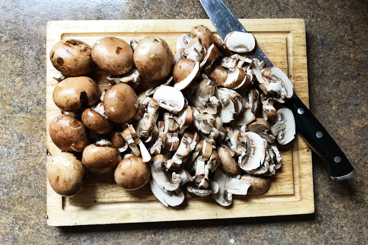 Brown cremini mushrooms, whole and sliced on wooden cutting board with knife