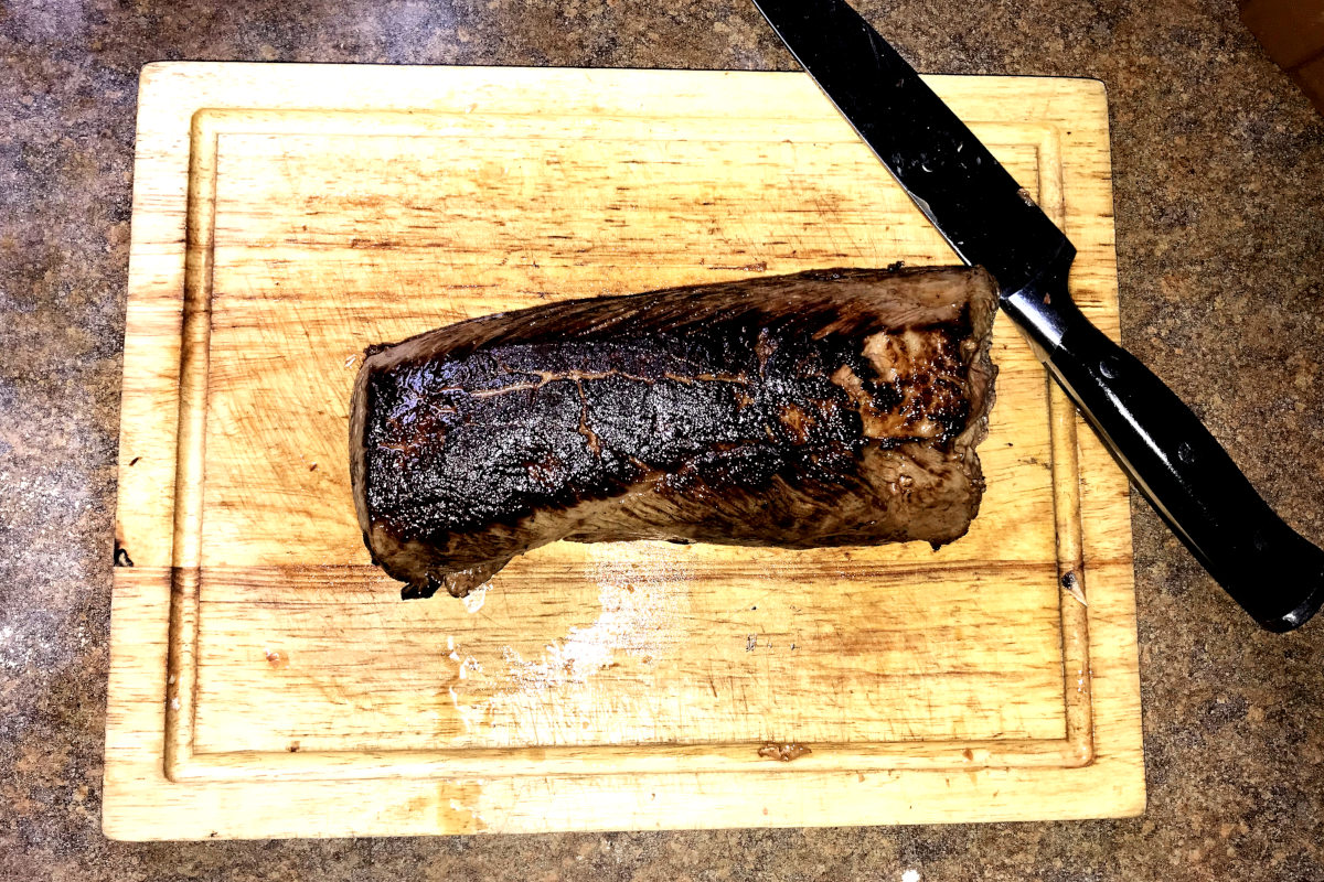 venison roast on wooden cutting board with knife