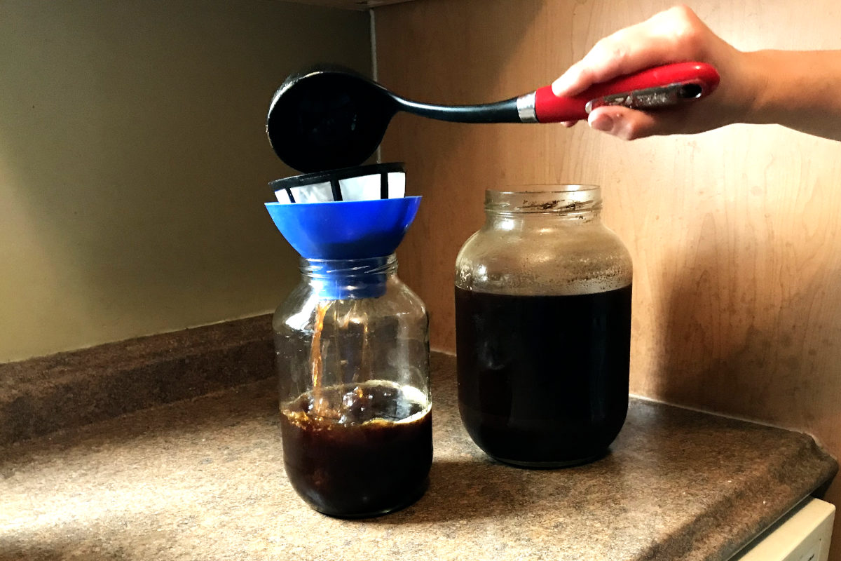 Pouring cold brew coffee through a reusable coffee filter into another jar