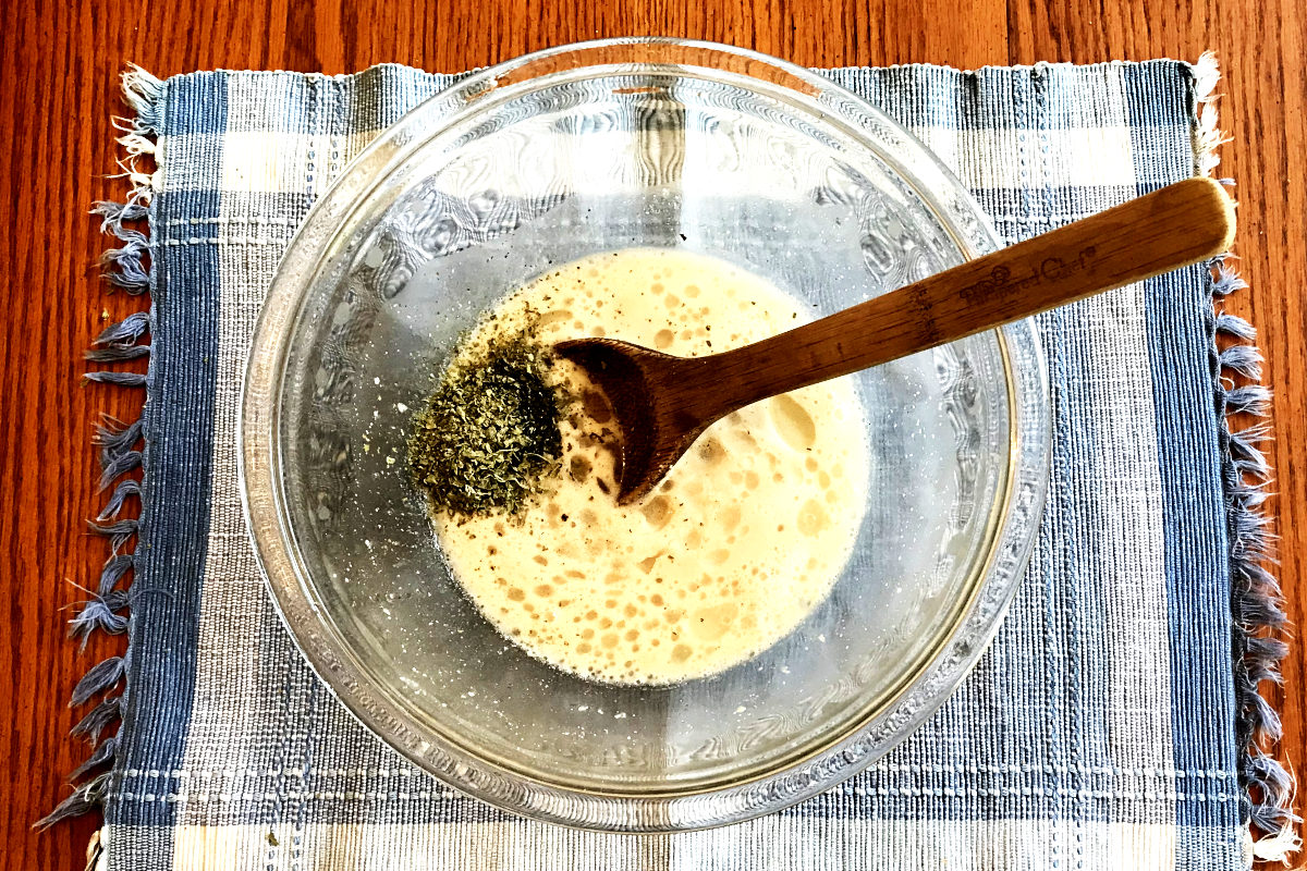 Yeast mixture with oil, salt and basil in a mixing bowl on a placemat