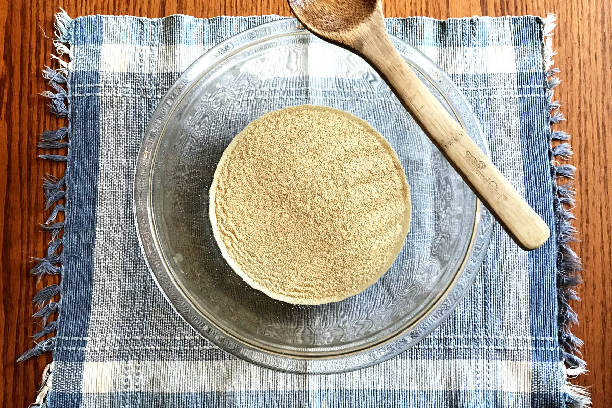 Yeast sprinkled over sugar water in mixing bowl on placemat