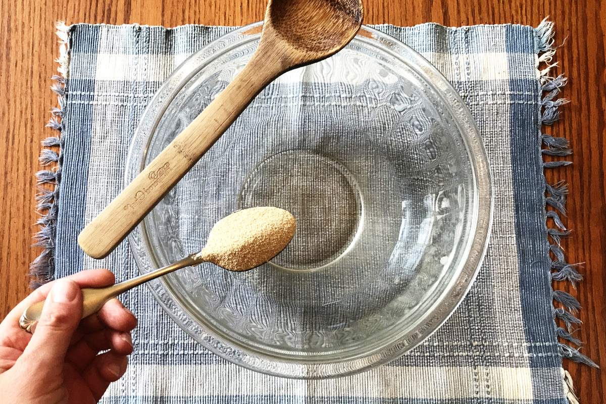 Yeast in spoon over a mixing bowl of sugar dissolved in water