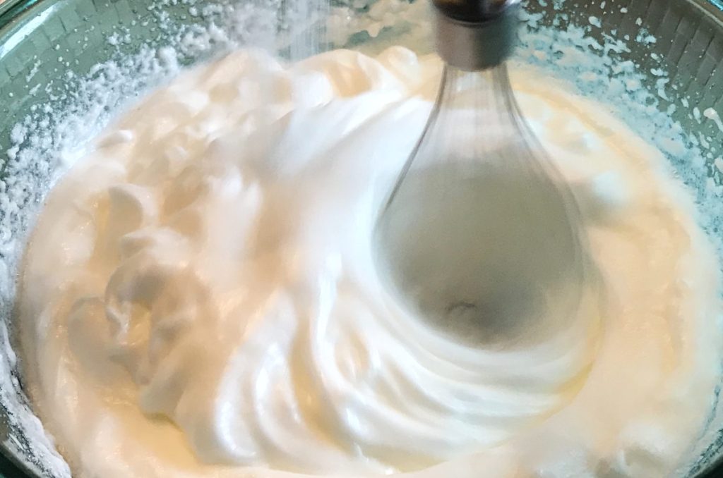 adding sugar to meringue during whipping with whisk blender in bowl