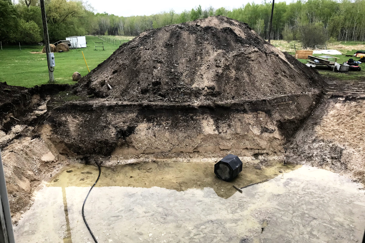 excavated basement hole with water covering the bottom and a large pile of dirt and gravel behind it. 