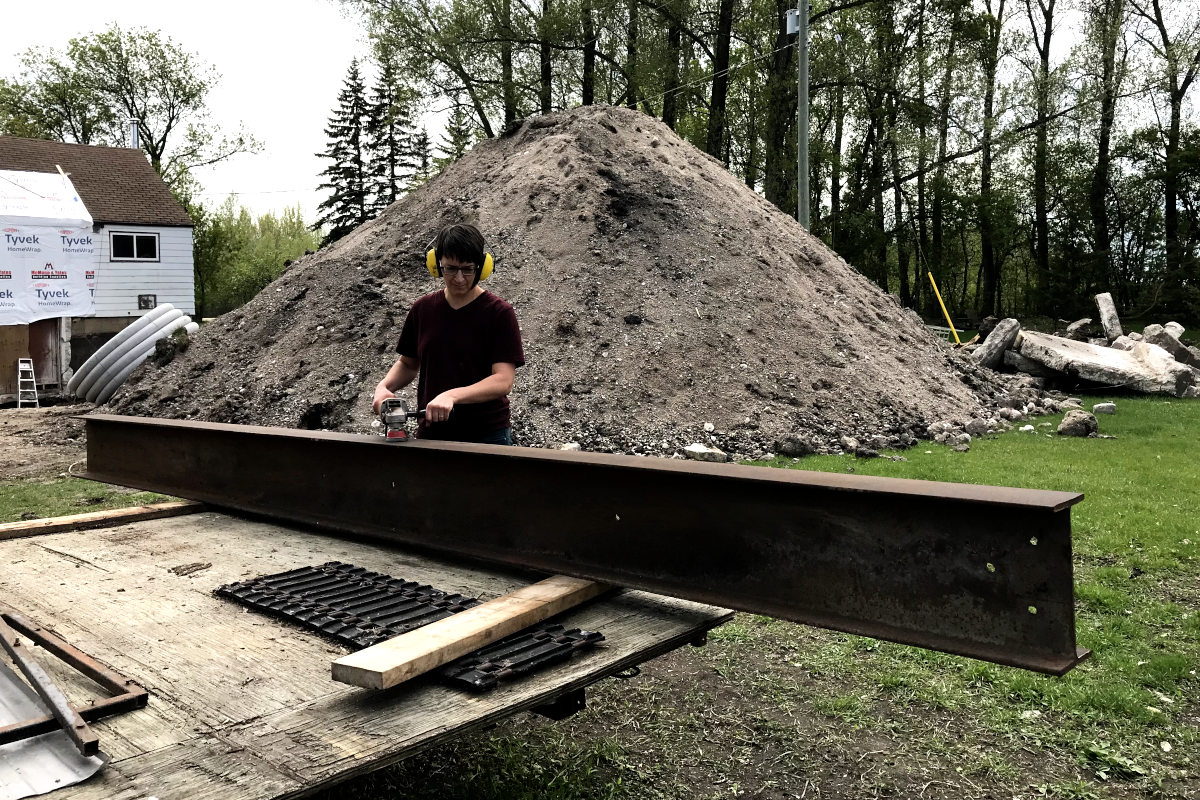 Grinding rust off of a 16 foot steel beam for our old house remodel, with gravel and dirt pile and old house in the background