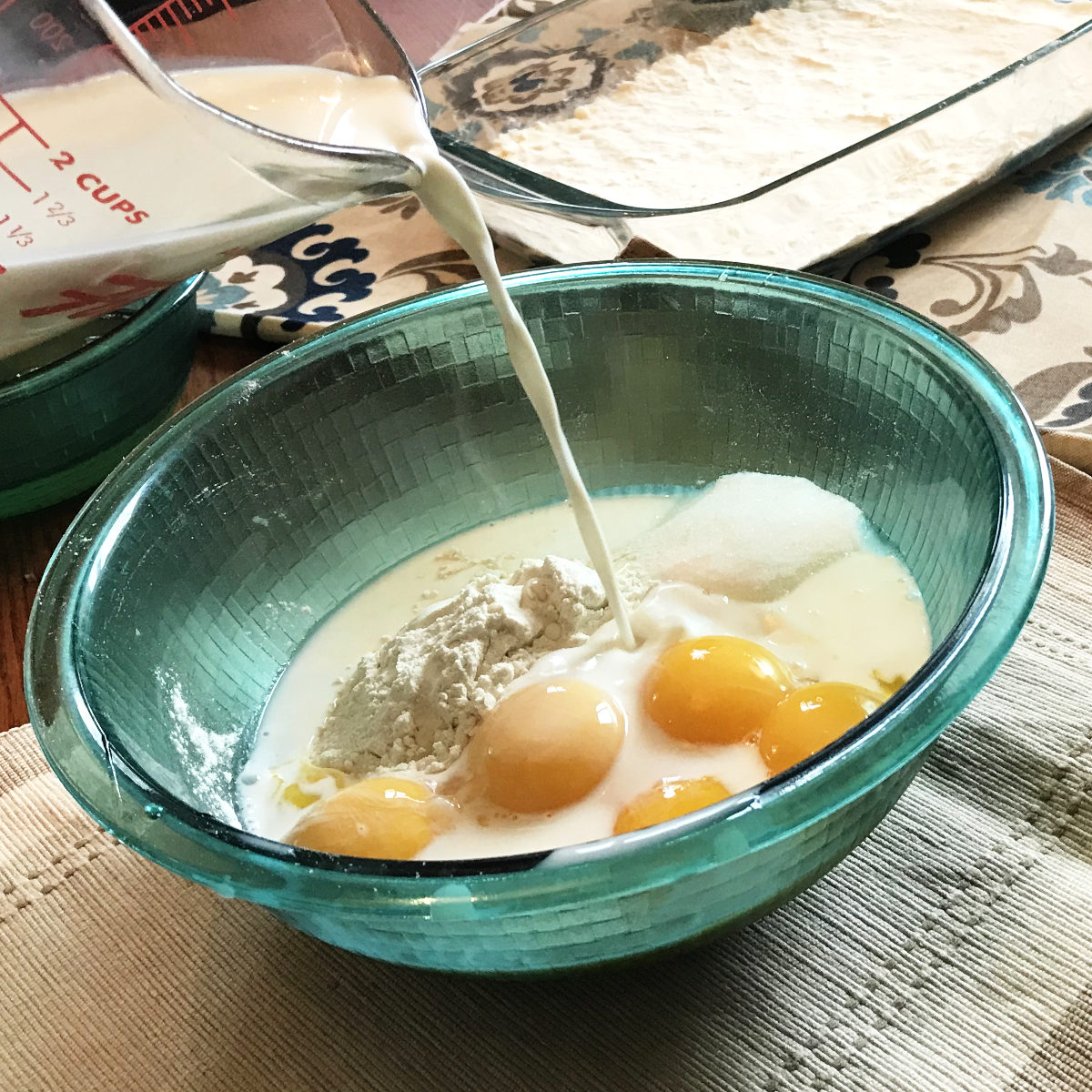 pouring milk into custard mixture in bowl