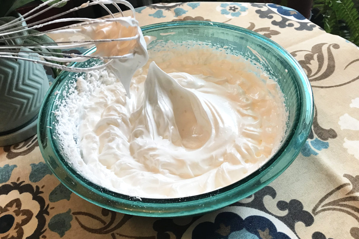 stiff peaks of meringue in bowl with whisk