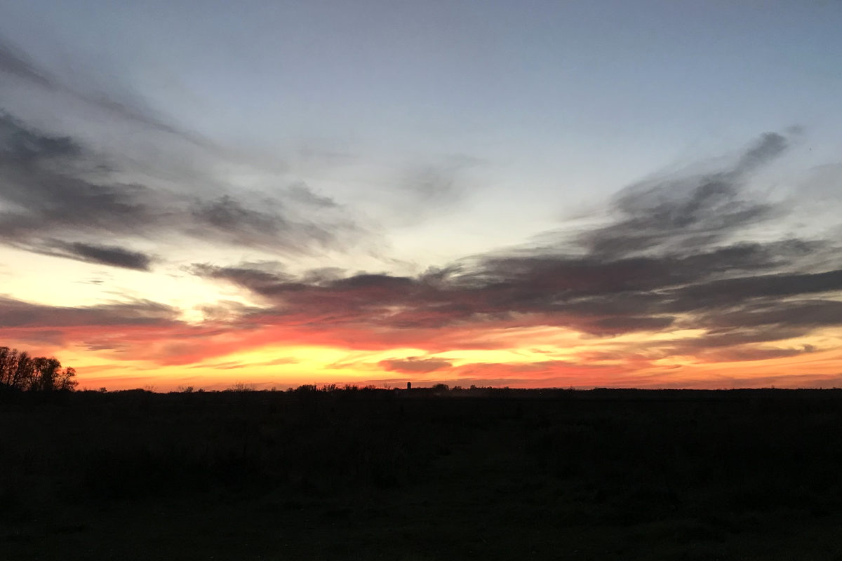 sunset over pasture and field with silo in the distance
