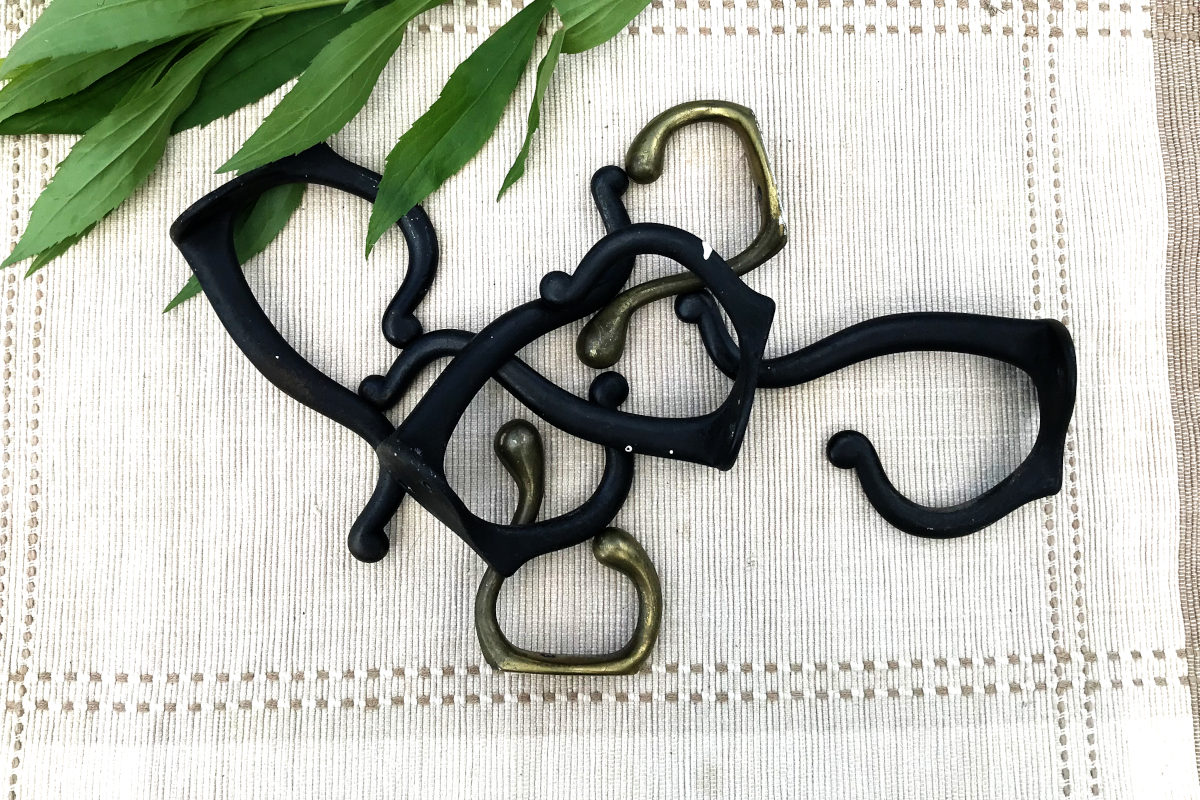 four big, curvy black hooks and two small brass hooks on placemat with leaves from old house remodel