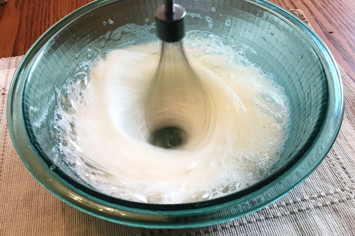 egg whites getting frothy during whipping in a bowl with whisk blender