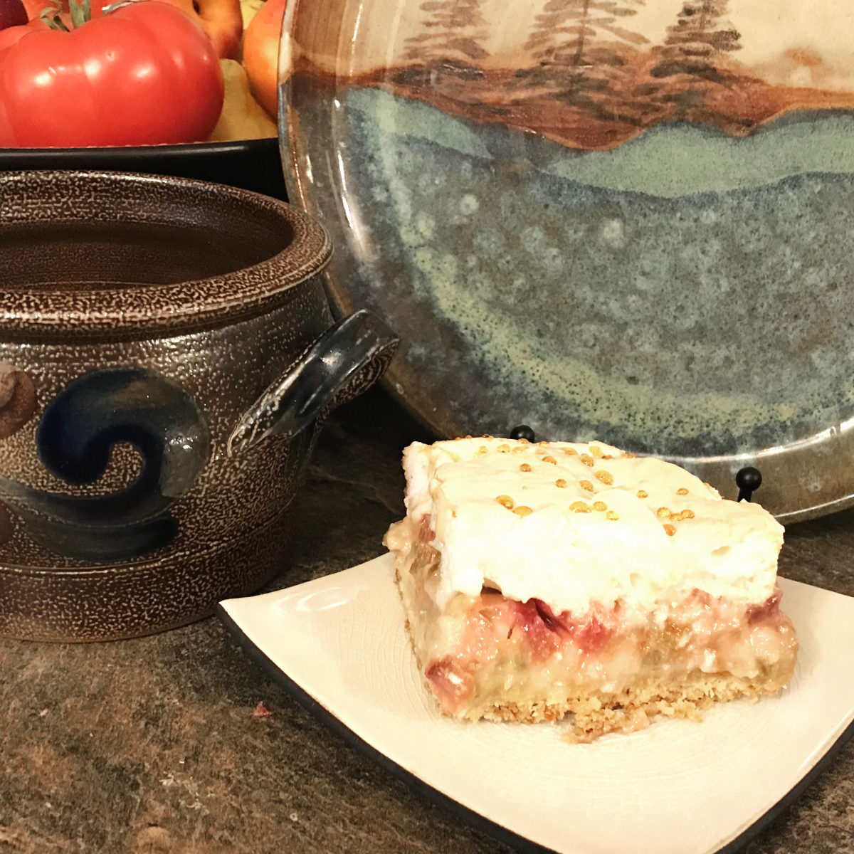 piece of rhubarb dessert on plate with pottery in background