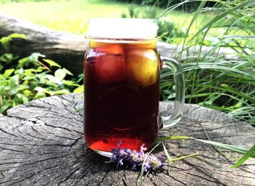 clear mug of homemade iced tea on a tree stump