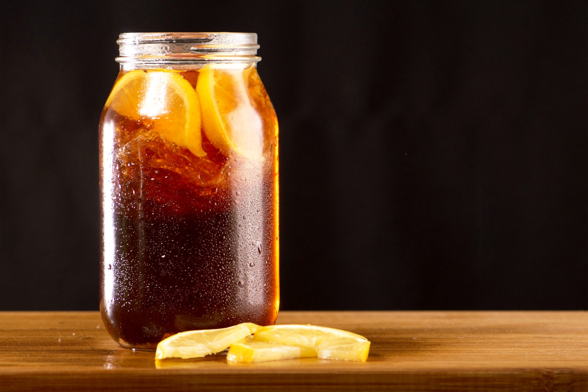 Jar of homemade iced tea with lemon slices all on a wooden cutting board with a black backdrop.