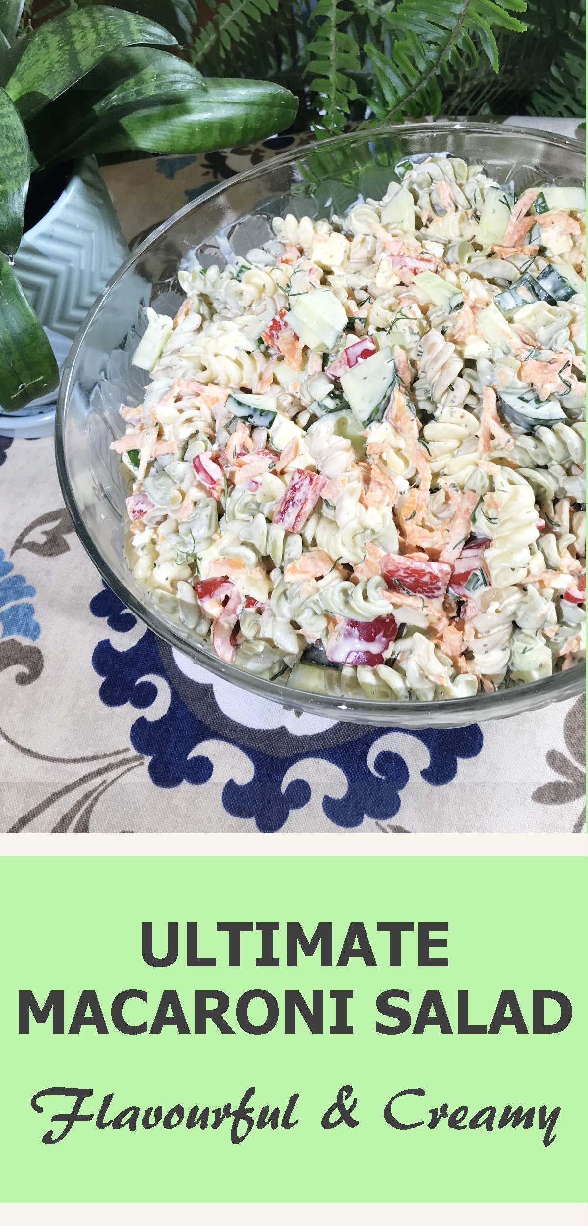 Glass serving bowl of ultimate macaroni salad on table cloth with plants with text reading ultimate macaroni salad, flavorful and creamy