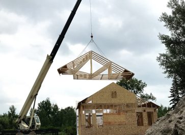 crane raising the roof trusses over the addition of the old house remodel