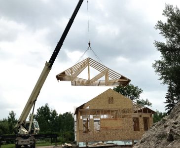 crane raising the roof trusses over the addition of the old house remodel