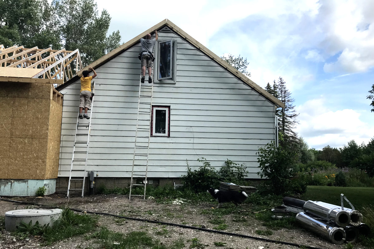 Two people on ladders attaching a eaves to the old roof of our old house remodel