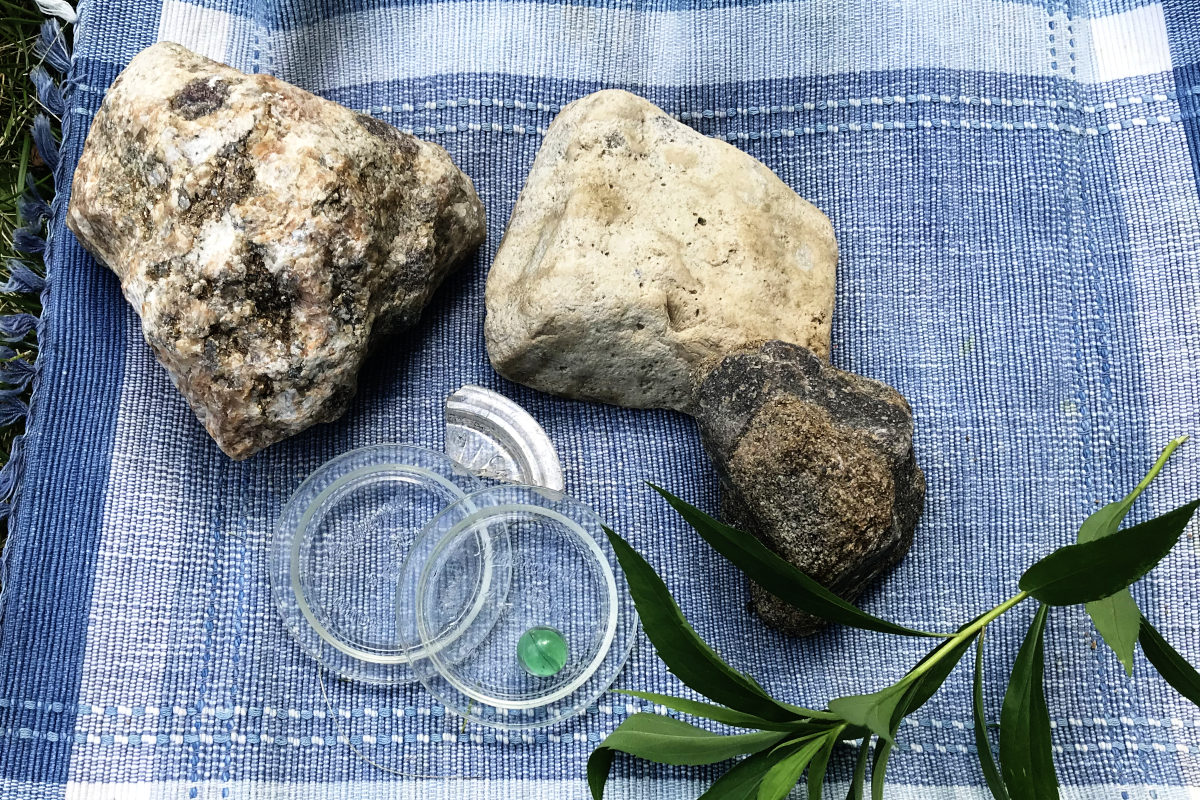 Sparkly rocks, rock with fossil, gem jar lids and marble found in the old house remodel dig site, on a placemat with a sprig of greenery