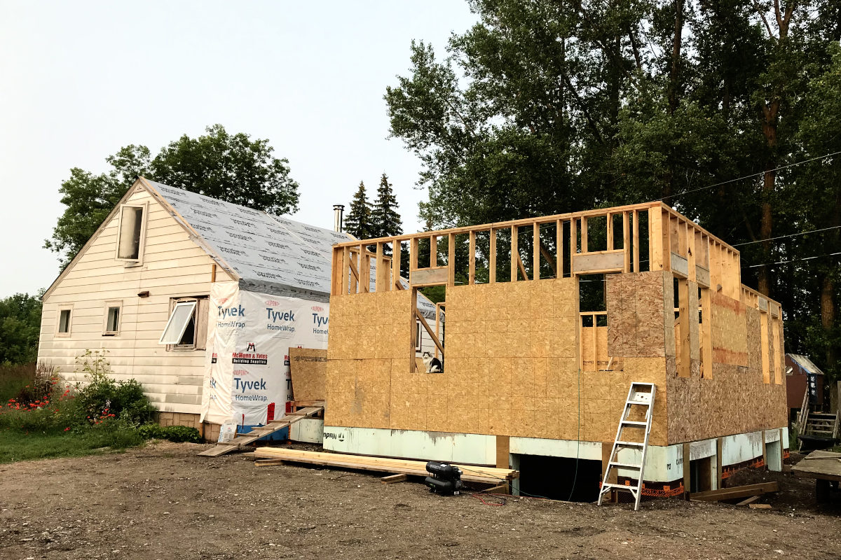 picture of old house and new addition with walls up. The old roof has been repaired again.