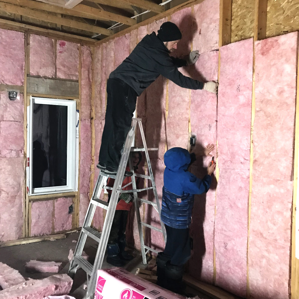 three people insulating walls with bat insulation
