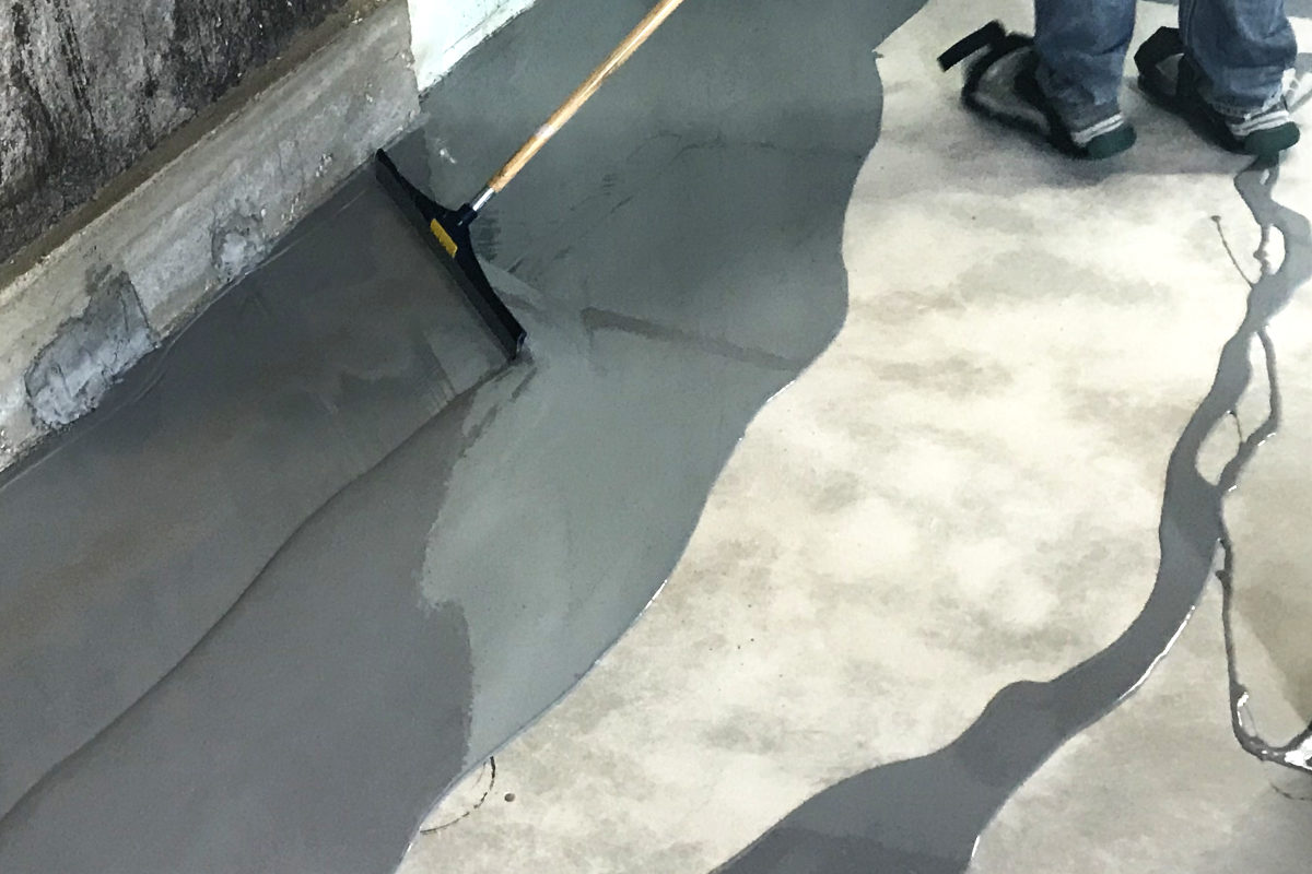 Squeegeeing epoxy onto concrete floor in old house remodel addition