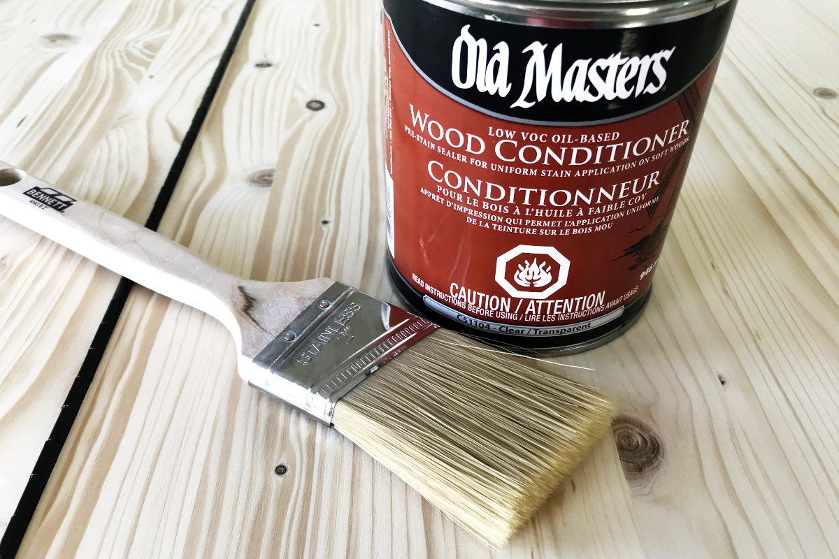 Can of Old Masters wood conditioner and a paint brush sitting on wood board