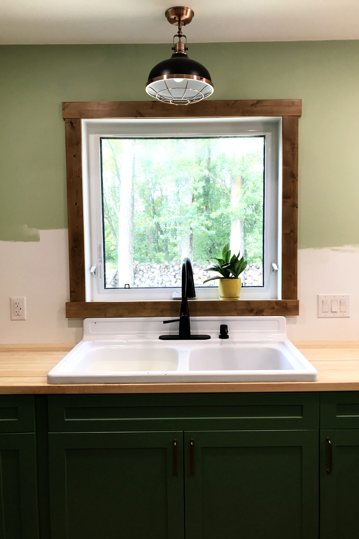 installed farmhouse enamel kitchen sink with butcher block counters, window, and green cabinets in our old house remodel.