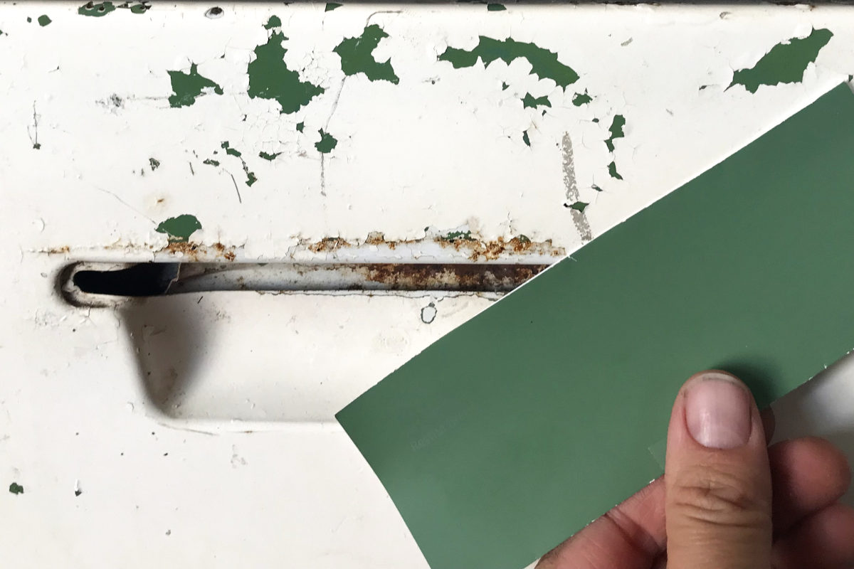 Paint chip from new kitchen cabinets a close match to the original green of the enamel sink's metal cabinet, seen under flaking white paint.