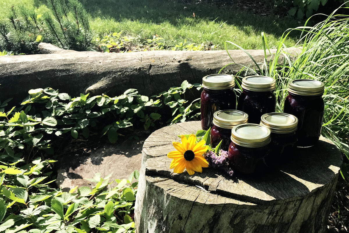 jars of chokecherry syrup on a stump with flowers surrounded by greenery