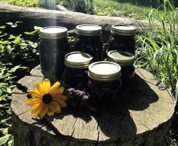 jars of chokecherry syrup on a stump with flowers
