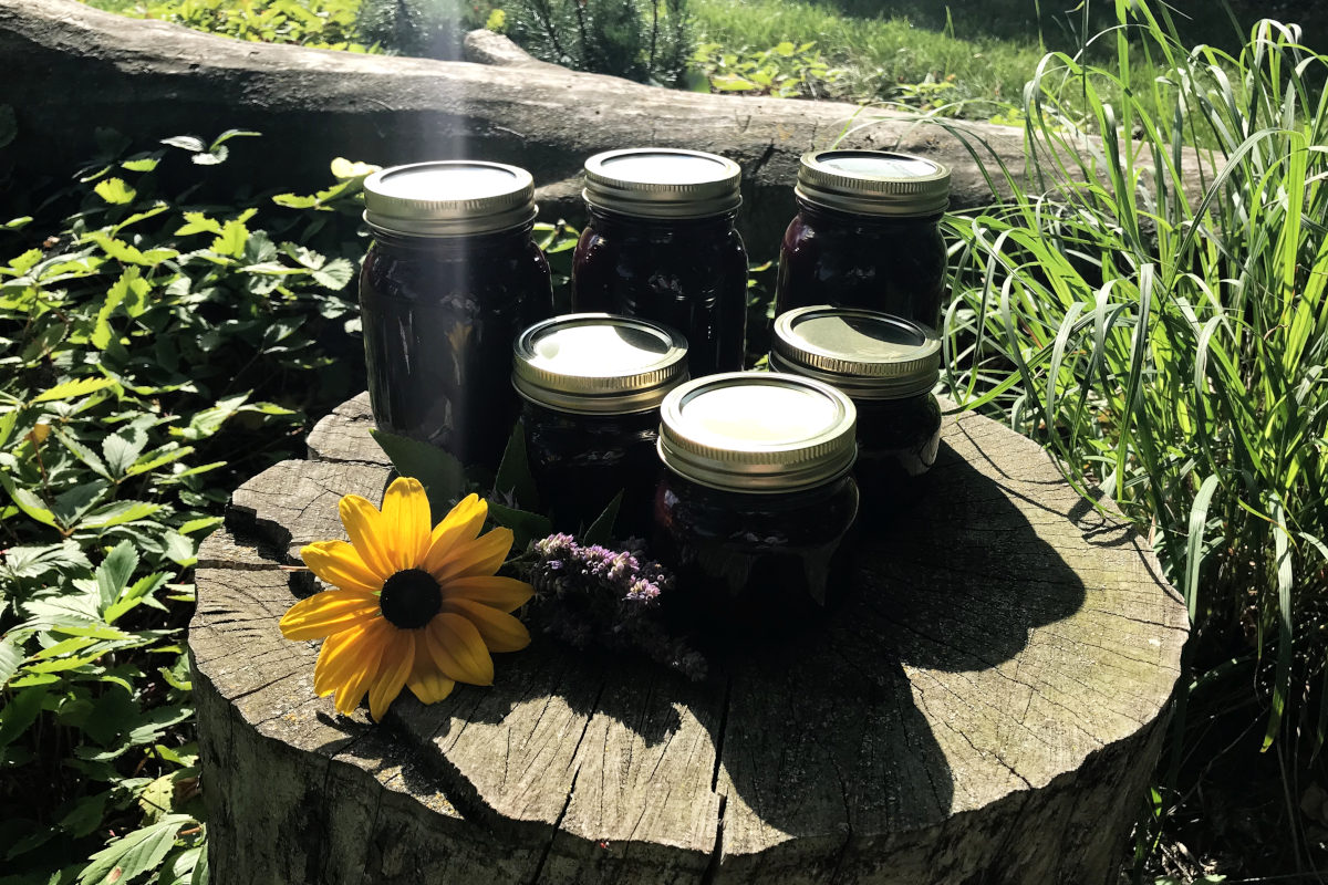 jars of chokecherry syrup on a stump with flowers