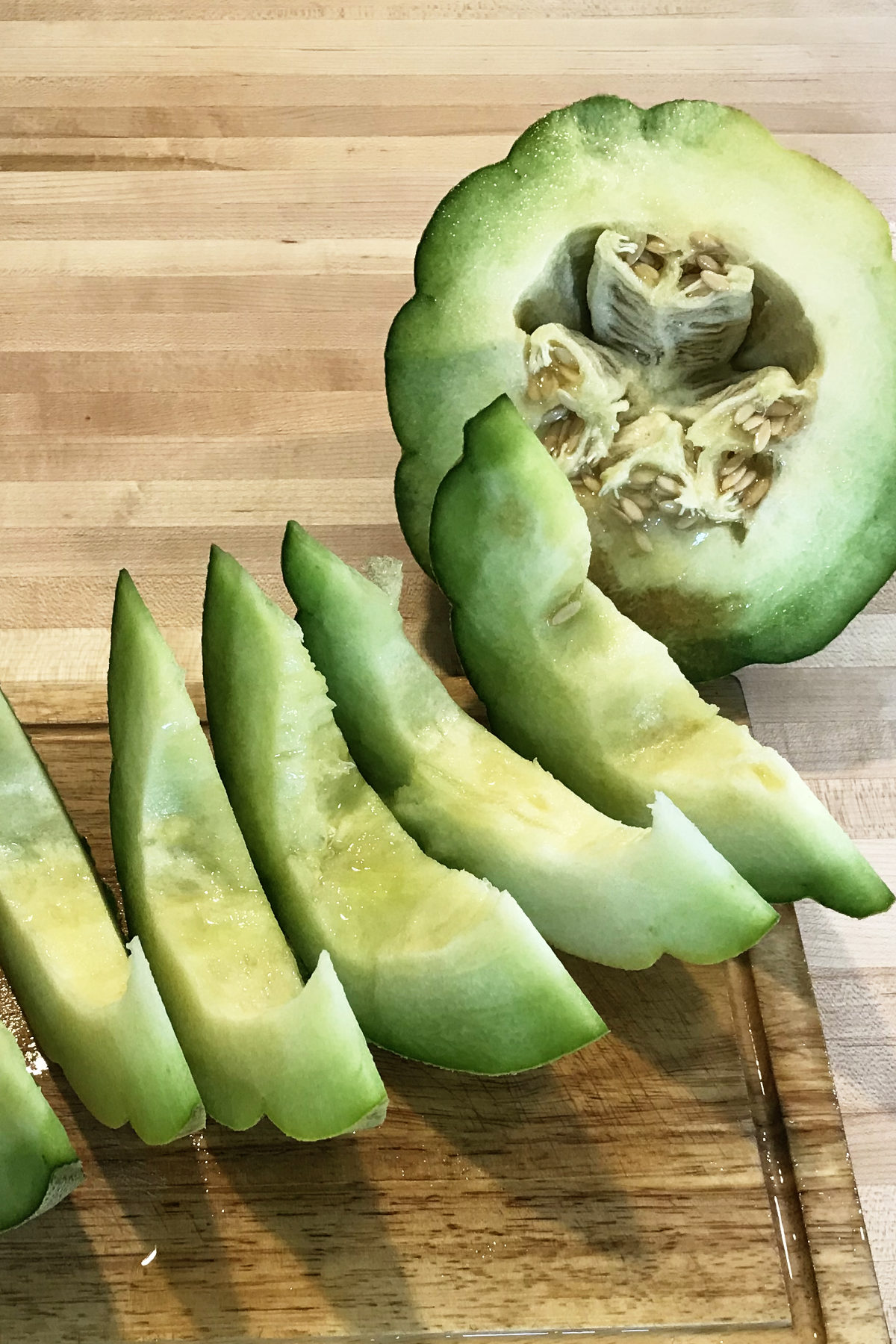 montreal market melon sliced in half with slices on the side, on a wooden cutting board, on butcher block counter