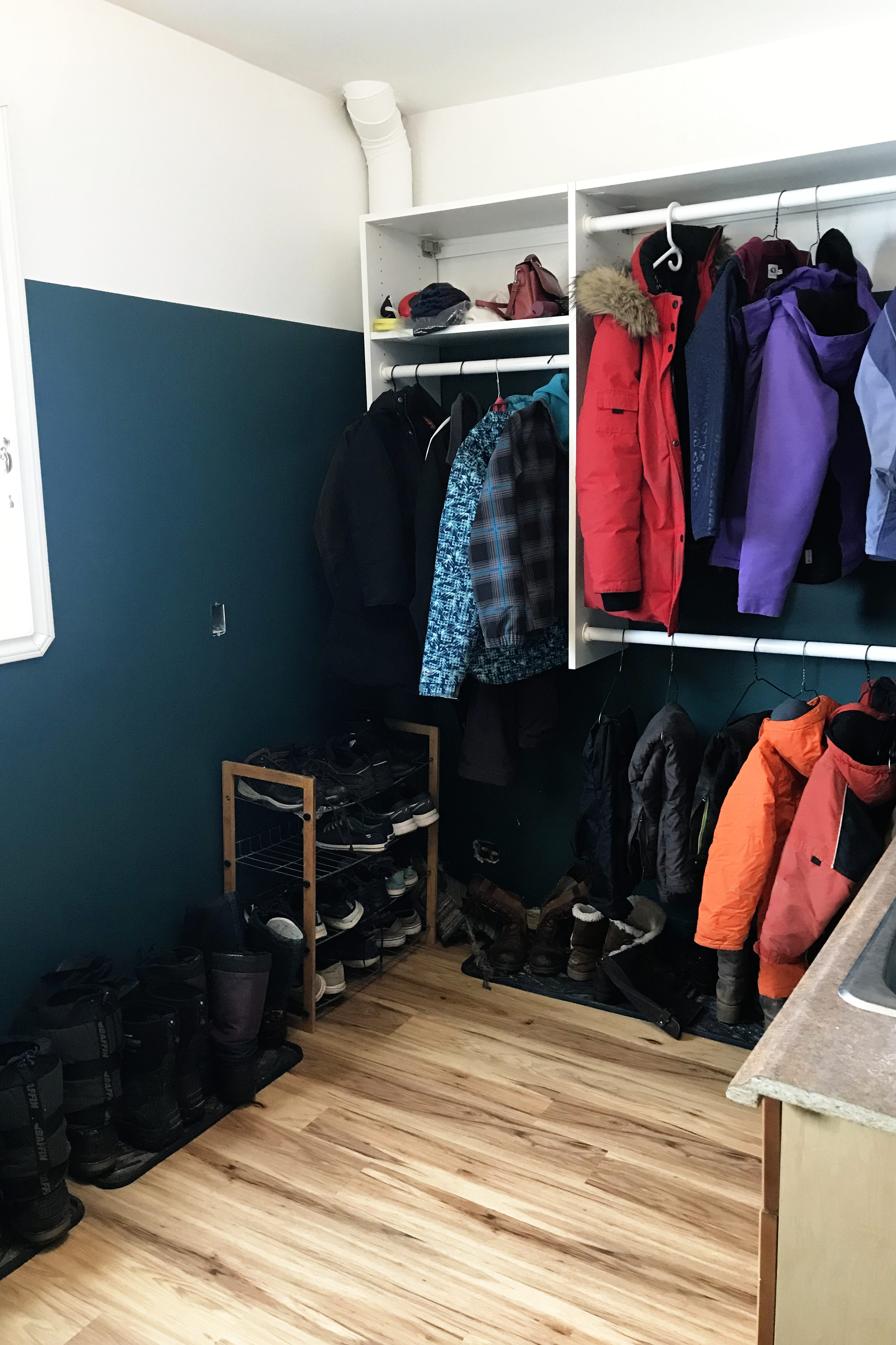 closet in mudroom with coats, teal paint 3/4 up the walls, white ceiling and upper walls, vinyl plank flooring, boots on trays, edge of a sink.