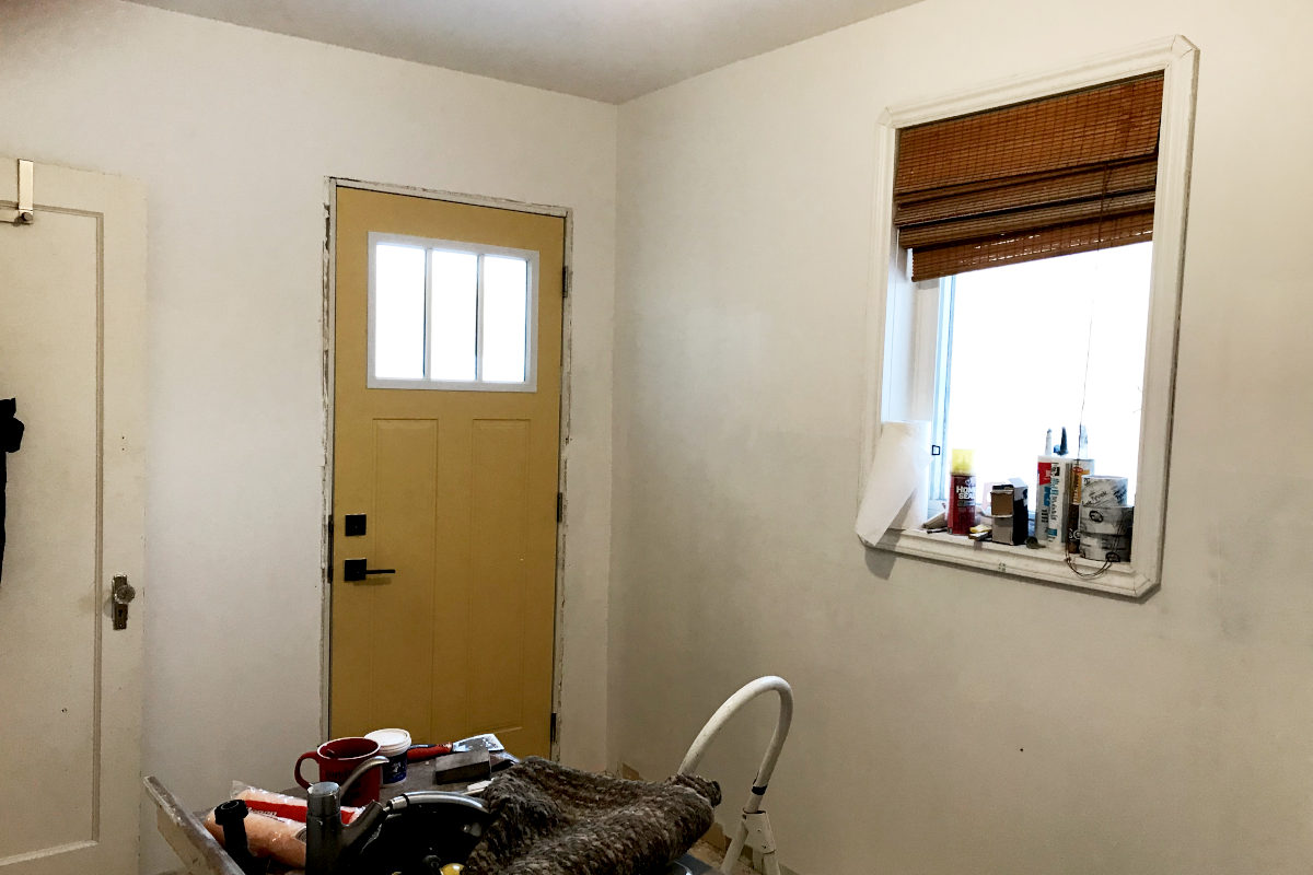 primed mudroom with exterior yellow door, and window. Renovation supplies lying around.