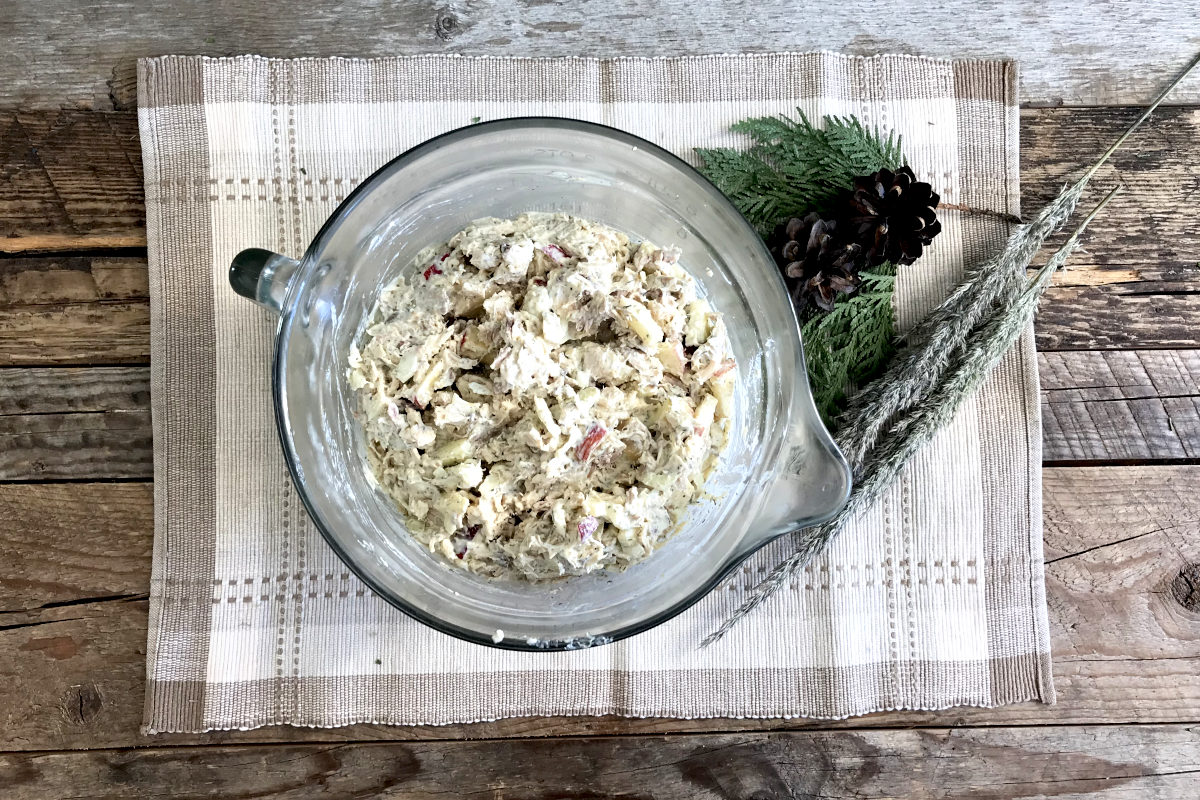 Measuring bowl of mixed chicken salad on a place mat with greenery on weathered wood