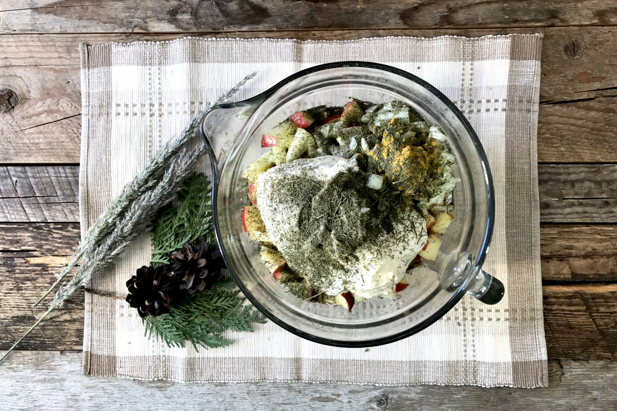 Homemade Chicken Salad ingredients in a large measuring bowl on a place mat with greenery on weathered wood