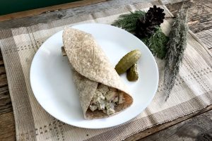homemade chicken salad tortilla wrap on a white plate on place mat with greenery on weathered wood