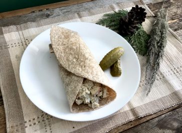 homemade chicken salad tortilla wrap on a white plate on place mat with greenery on weathered wood