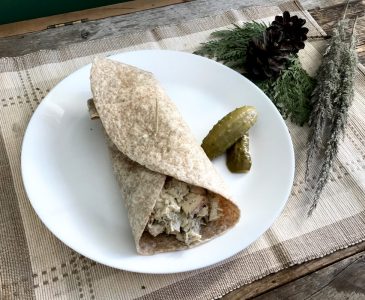 homemade chicken salad tortilla wrap on a white plate on place mat with greenery on weathered wood