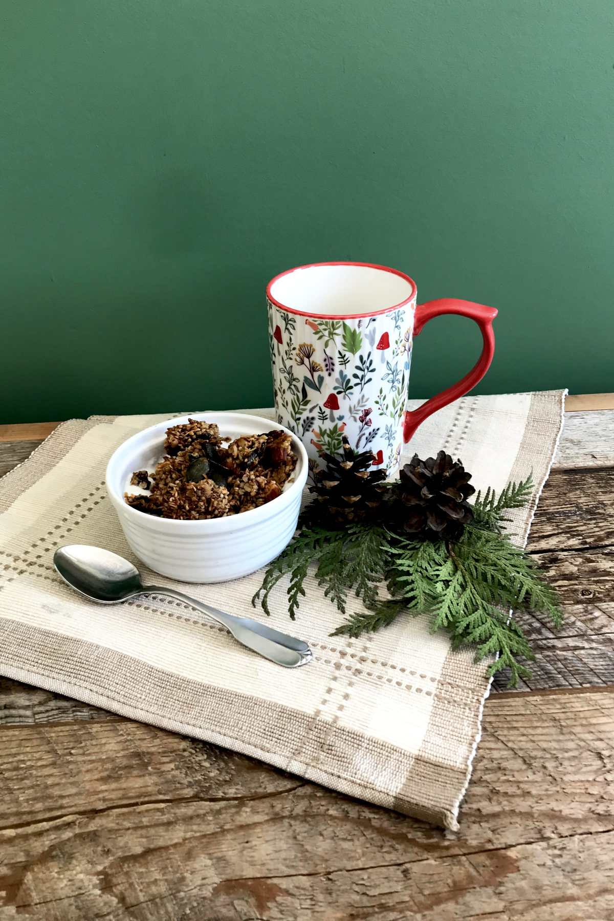 bowl of granola on place mat with mug and greenery on weathered wood