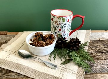 homemade granola in a bowl on a place mat with a mug and greenery on weathered wood