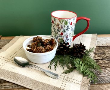 homemade granola in a bowl on a place mat with a mug and greenery on weathered wood