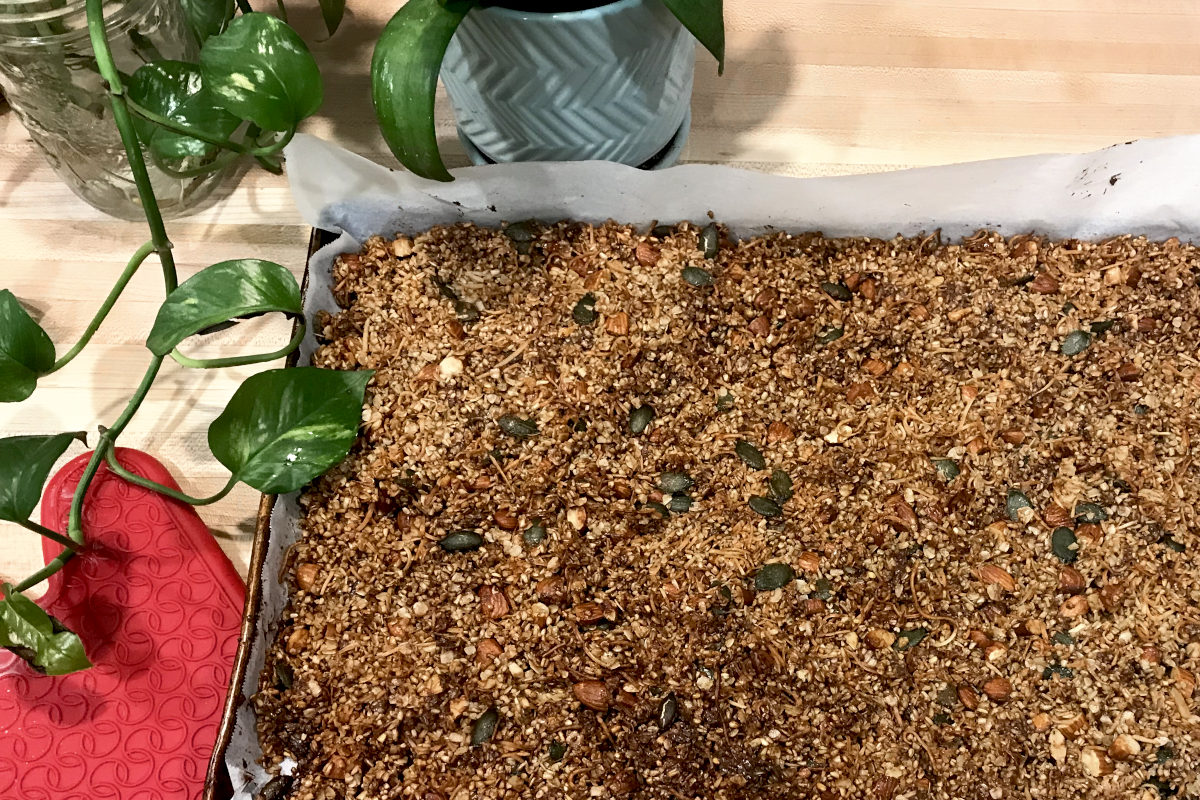 baked homemade granola in a baking sheet with greenery and oven mitt on butcher block counter
