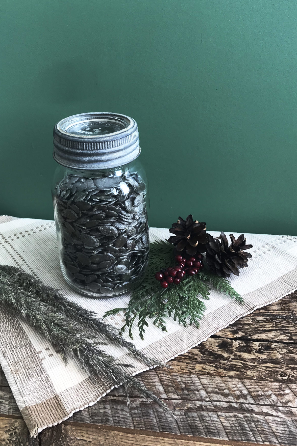 jar of hulless pumpkin seeds on place mat on weathered wood with greenery