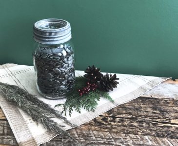 jar of hulless pumpkin seeds on placemat on weathered boards with greenery